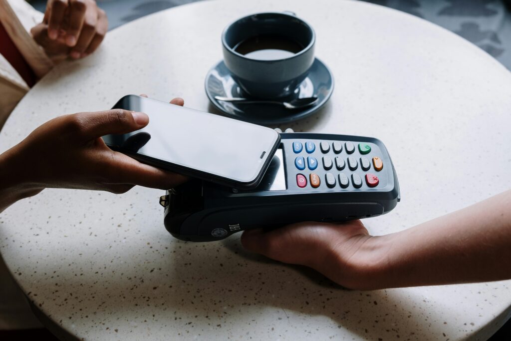 A person using a smartphone to make a contactless payment with a card reader on a cafe table.